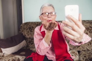 Senior old woman sending love and kisses to her family over skype or viber using her cellphone